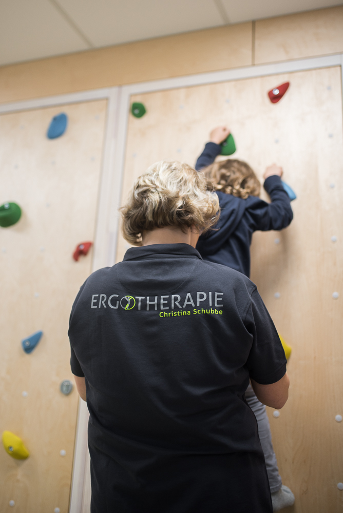 Ergotherapeutin begleitet ein Kind an der Kletterwand
